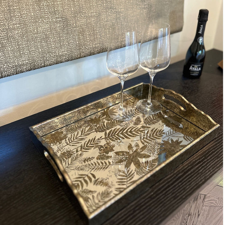 Round, antique gold rimmed tray with a mirrored sunburst pattern, styled on a coffee table with drinks and decor in a cozy living room.