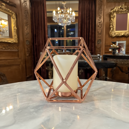 Geometric rose gold candle holder with a white candle on a marble surface in an elegant room.