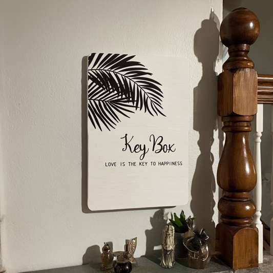 Decorative key box with leaf design and text on a wall next to wooden furniture.