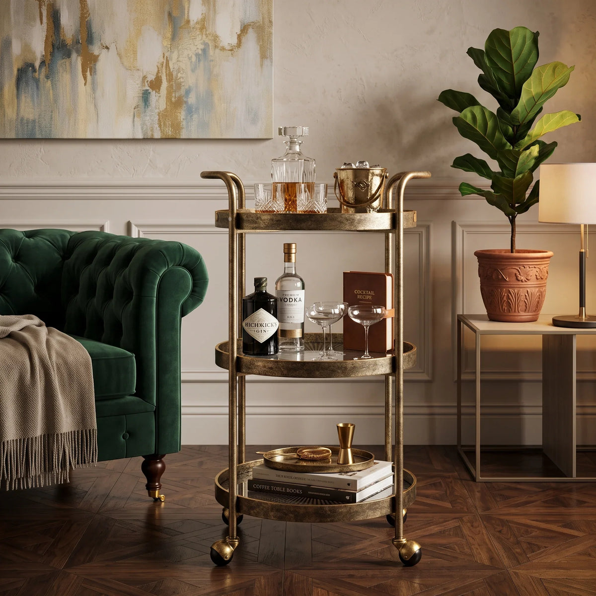 A three-tier rolling bar cart with a distressed gold finish stands in a styled living room. The cart is styled with a decanter, glasses, a metal caddy, a bottle of absinthe .