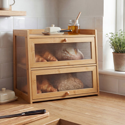 Wooden bread bin with glass panels containing loaves of bread in a kitchen setting.