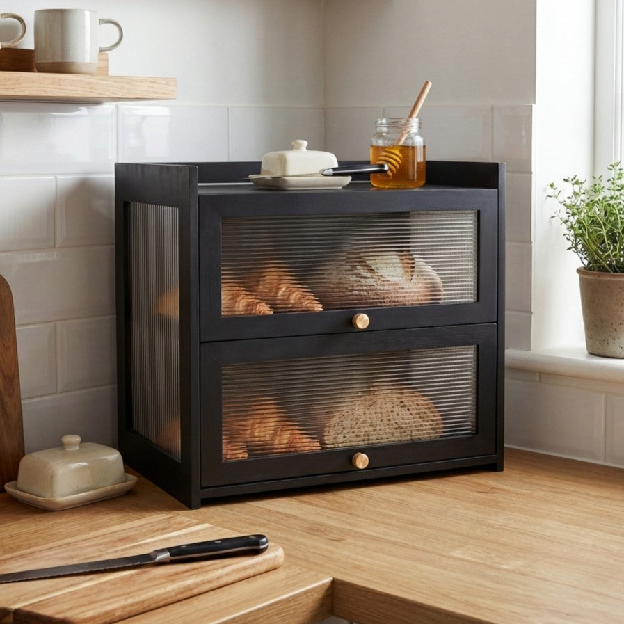 Black bread bin with glass doors displaying loaves of bread in a kitchen setting.
