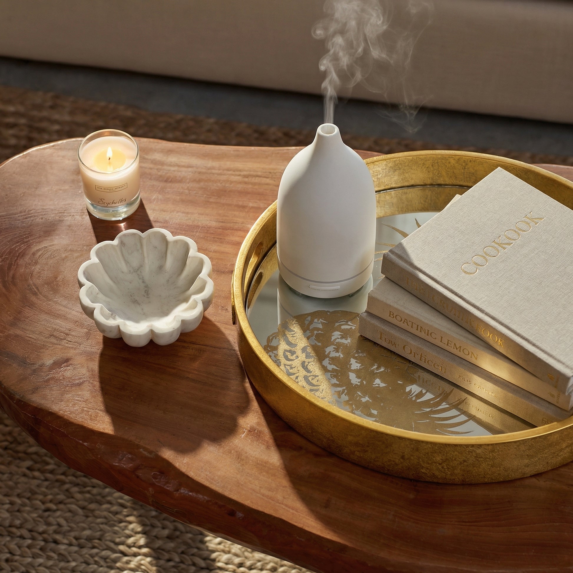 Decorative items on a wooden table including a candle, shell dish, white vase, and books.