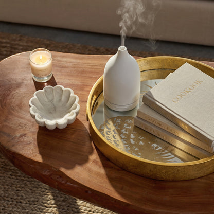 Decorative items on a wooden table including a candle, shell dish, white vase, and books.