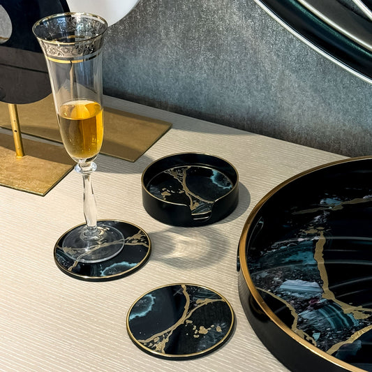 Glass of champagne on a coaster with decorative coasters and a tray on a table.